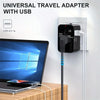 Schwarzer universeller Reiseadapter mit USB-Anschluss, eingesteckt in eine weiße Steckdose neben einem Laptop.
