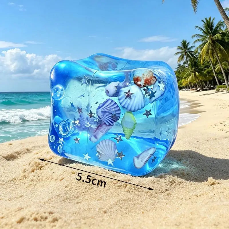 A translucent blue squeeze toy shaped like an ocean creature resting on a sandy beach near the sea.