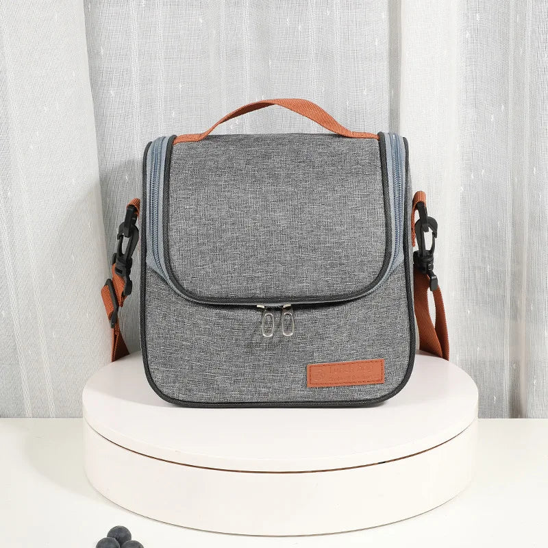A gray insulated lunch bag with an orange strap is displayed on a white stand.