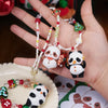 A hand holds a blind box panda figure and beaded bracelets in front of a Christmas tree decoration.
