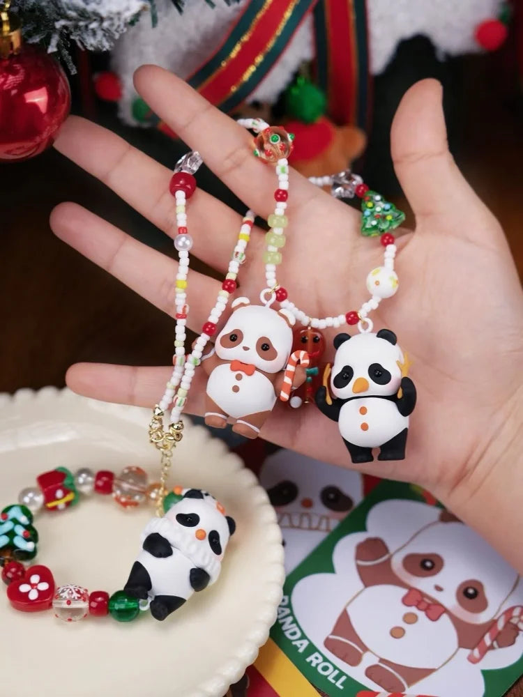 A hand holds a blind box panda figure and beaded bracelets in front of a Christmas tree decoration.
