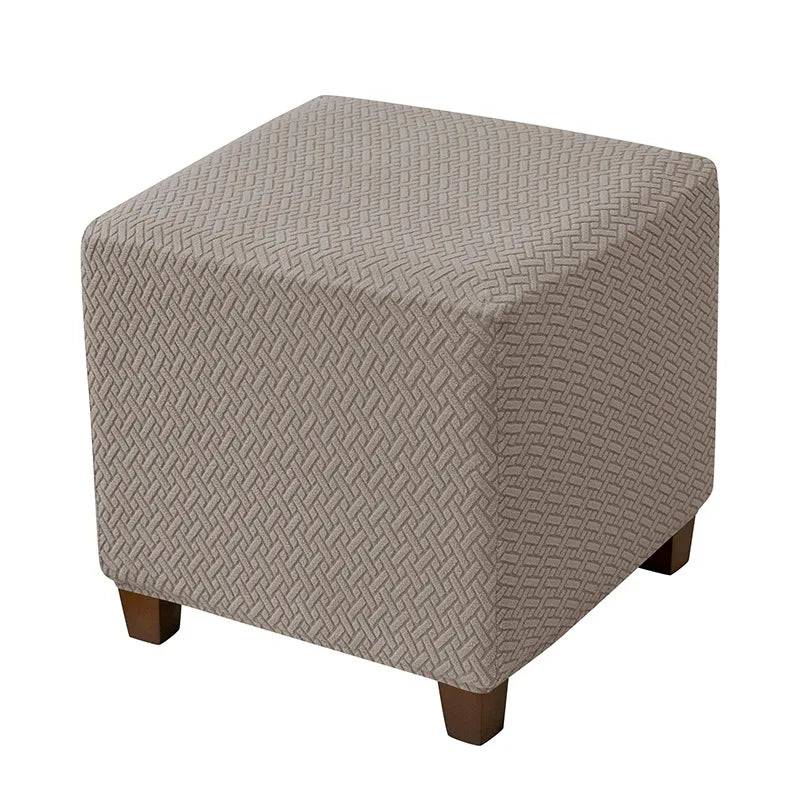 A square ottoman slipcover in a light taupe color with a textured diamond pattern.