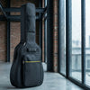 A black water-resistant acoustic guitar gig bag with padded protection standing on a gray floor.