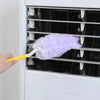 A hand is using a yellow tool to clean the interior of a white appliance with a purple feather duster.