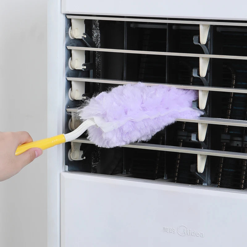 A hand is using a yellow tool to clean the interior of a white appliance with a purple feather duster.