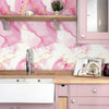 Pink marble pattern self-adhesive wallpaper roll applied to kitchen cabinets and shelving.