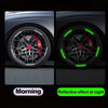 Close-up of a black alloy wheel with red brake calipers and green reflective stickers on the spokes.