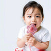 A baby is holding a pink teething rattle with a chewable gripper and shaker toy.