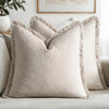 A beige linen throw pillow with fringed edges resting on a light-colored sofa.