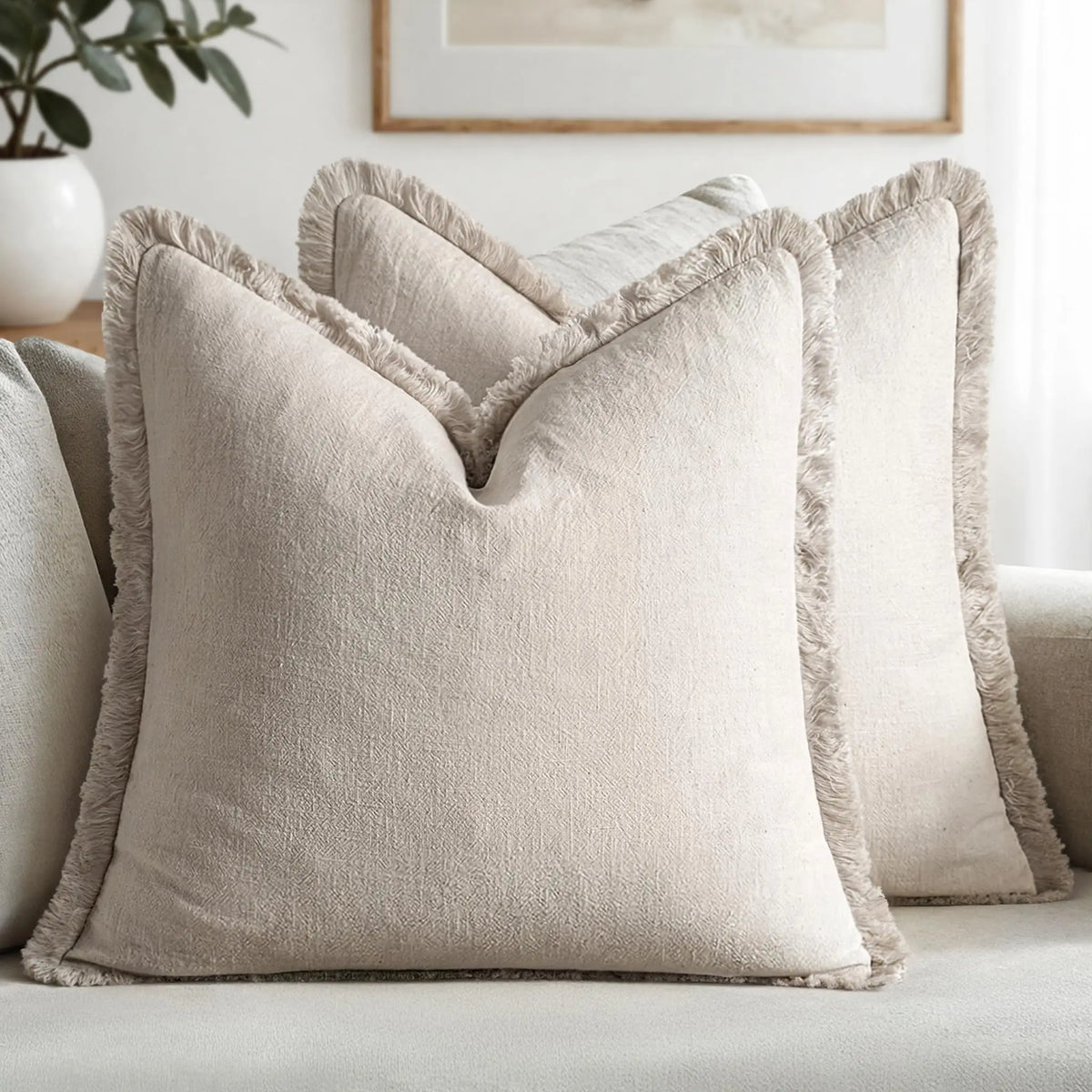A beige linen throw pillow with fringed edges resting on a light-colored sofa.