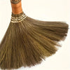 A handmade natural grass broom with a woven handle and light brown bristles is shown in a close-up view.