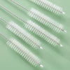 A set of reusable straw and bottle cleaning brushes with white bristles arranged diagonally on a light green surface.
