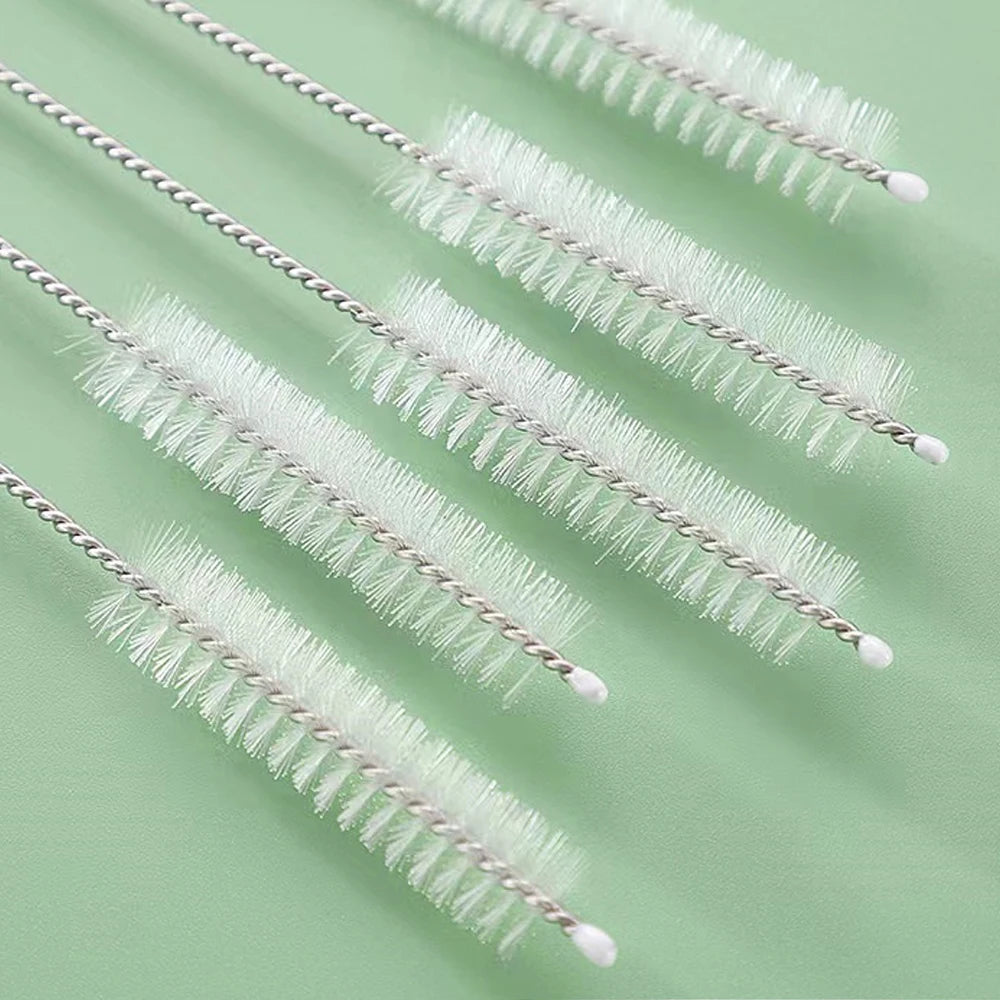 A set of reusable straw and bottle cleaning brushes with white bristles arranged diagonally on a light green surface.