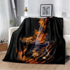 A black flannel throw blanket featuring a graphic design of an electric guitar engulfed in orange flames.