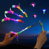 A hand launches an LED glowing flying arrow toy with a rubber band launcher against a dark night sky.