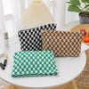 Three plaid makeup bags in black, brown, and green are displayed on a white table next to a light fixture.