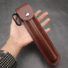 A brown leather holster for a manual wood auger drill is held in a hand against a dark gray background.
