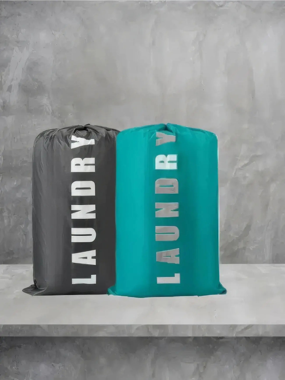 Two reusable laundry storage bags, one black and one teal, standing on a light gray shelf.