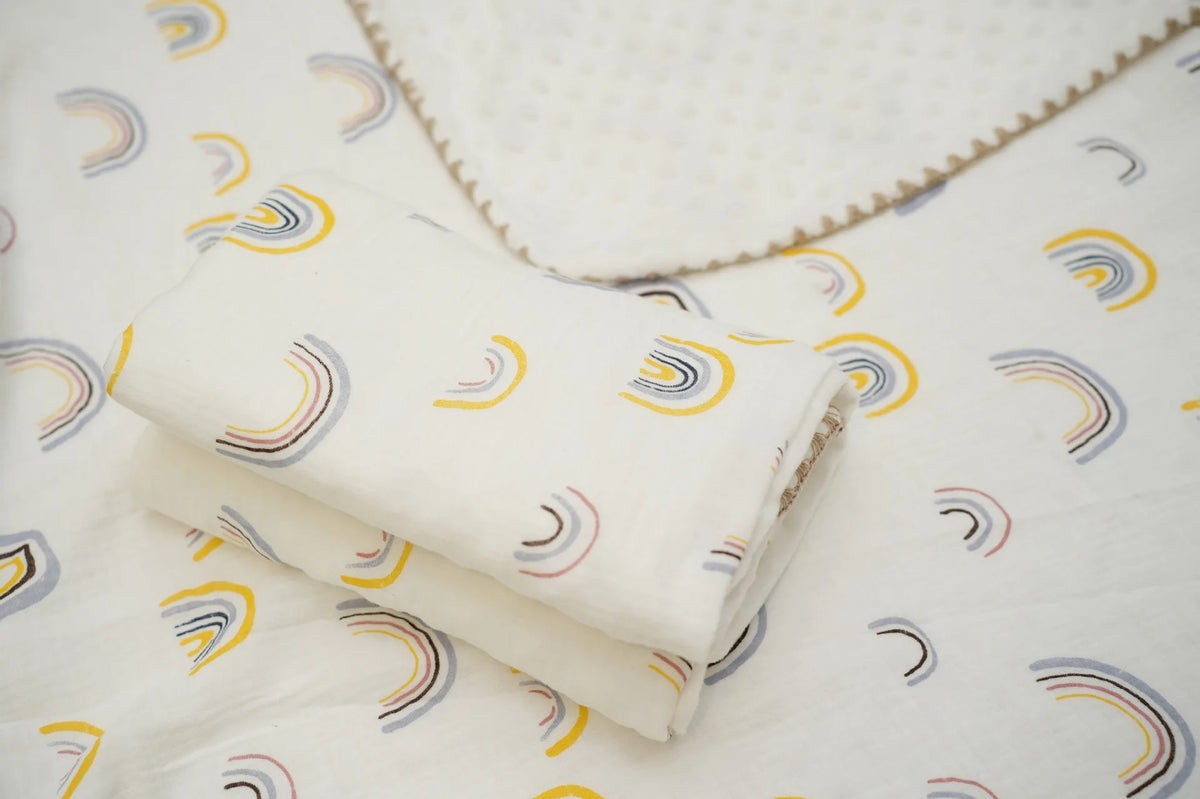 A rolled white cotton gauze baby swaddle blanket with a bear print pattern lying on a white fabric background.