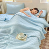 A light blue breathable waffle-weave summer quilt is spread on a bed, with a cup and saucer nearby.
