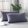 A set of two soft gray microfiber pillowcases resting on a white surface with greenery in the background.