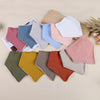 A collection of soft cotton baby bibs in various pastel colors including pink, blue, green, and beige, displayed on a light b
