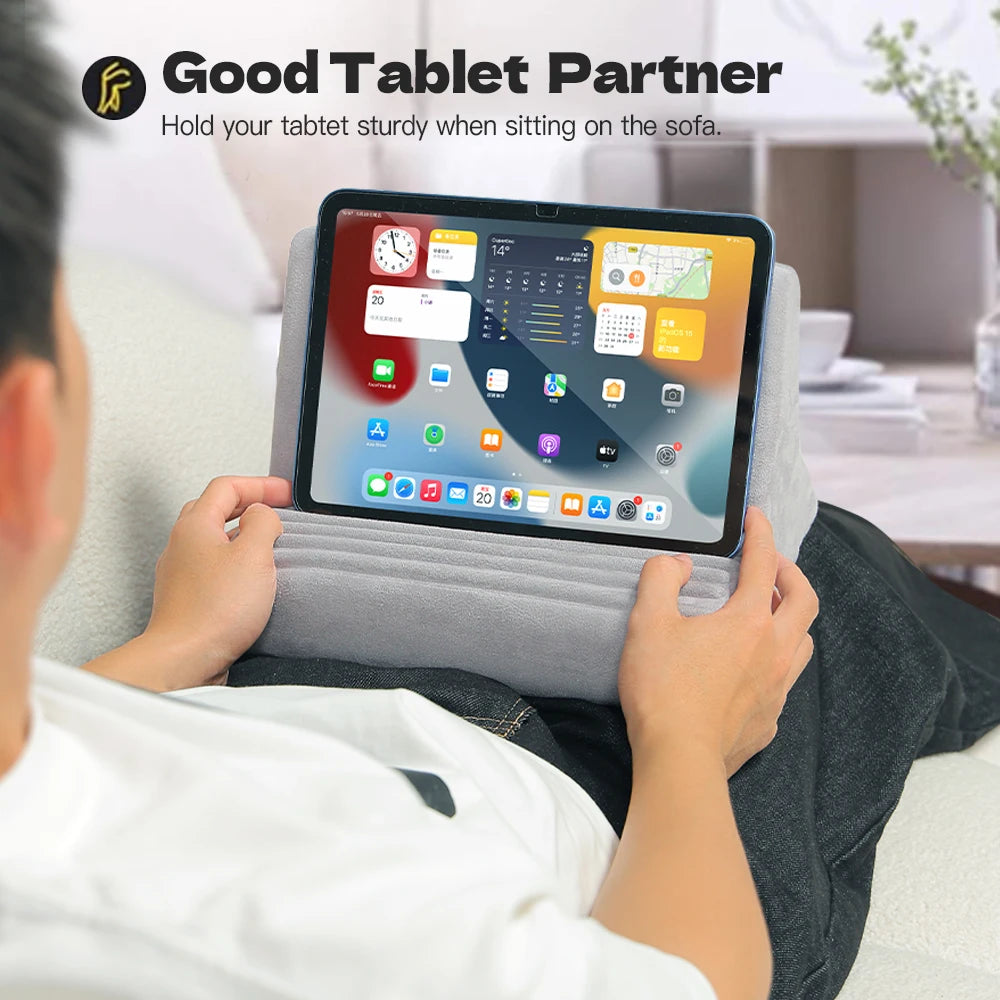 A person is holding a tablet in an adjustable comfort stand pillow while sitting on a sofa.