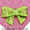 A set of five lime green sequin bow patches for DIY crafts displayed on a pink grid background.
