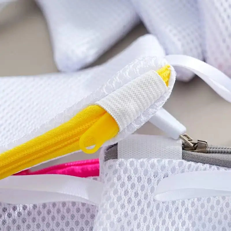 A close-up of white mesh laundry bags with yellow zippers and pink accents.