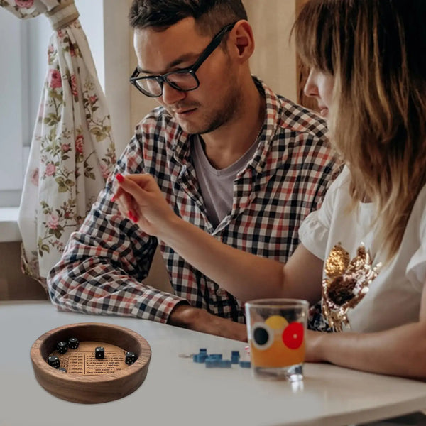 Une personne roule un jeu de dés classique en facettes avec un plateau en bois sur une table.