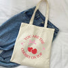 A beige canvas tote bag with pink cherry embroidery that reads You are the cherry on top, resting on a denim shirt.