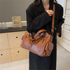 A woman holds a brown vintage leather tote bag with multiple pockets in a dark outfit.