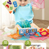 A baby holds a pink silk scarf and a colorful cloth book toy featuring cartoon animals.