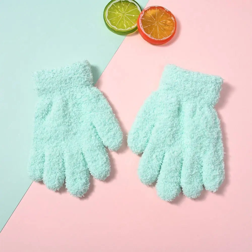 Pair of light mint green plush winter gloves resting on a pink background with citrus fruit.