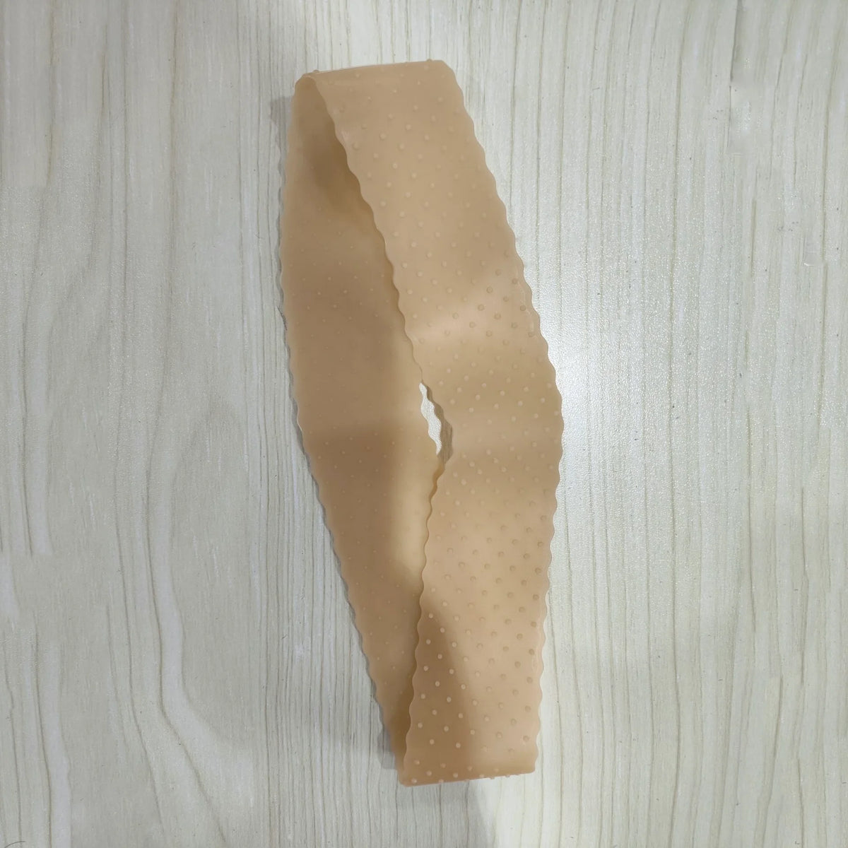 Beige Silikon-Perücken-Griffband mit strukturierter Oberfläche, liegt auf Holz.