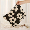 A hand holds a black and cream floral corduroy makeup bag with a secure zipper.