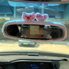 Pink plush bear and heart shaped love mirror covers placed on a car's rearview mirror.