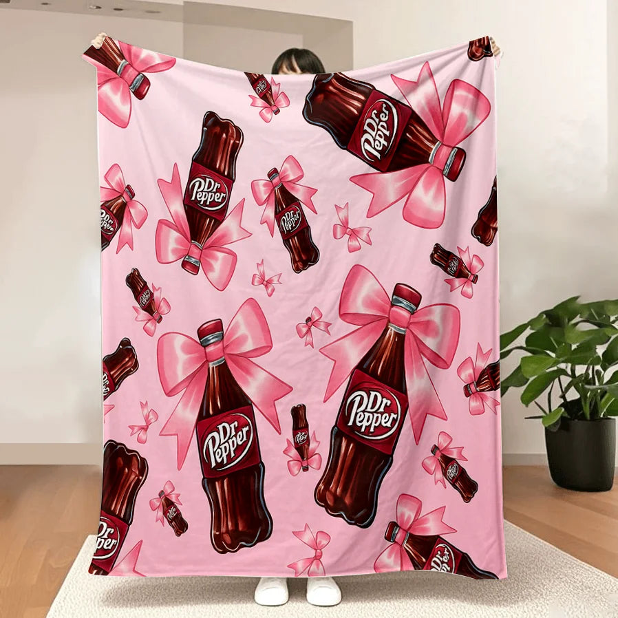 A pink throw blanket featuring a repeating pattern of Dr. Pepper bottles with pink ribbons.