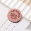 A round, pink felt label with the words handmade and a heart design resting on a piece of white paper.