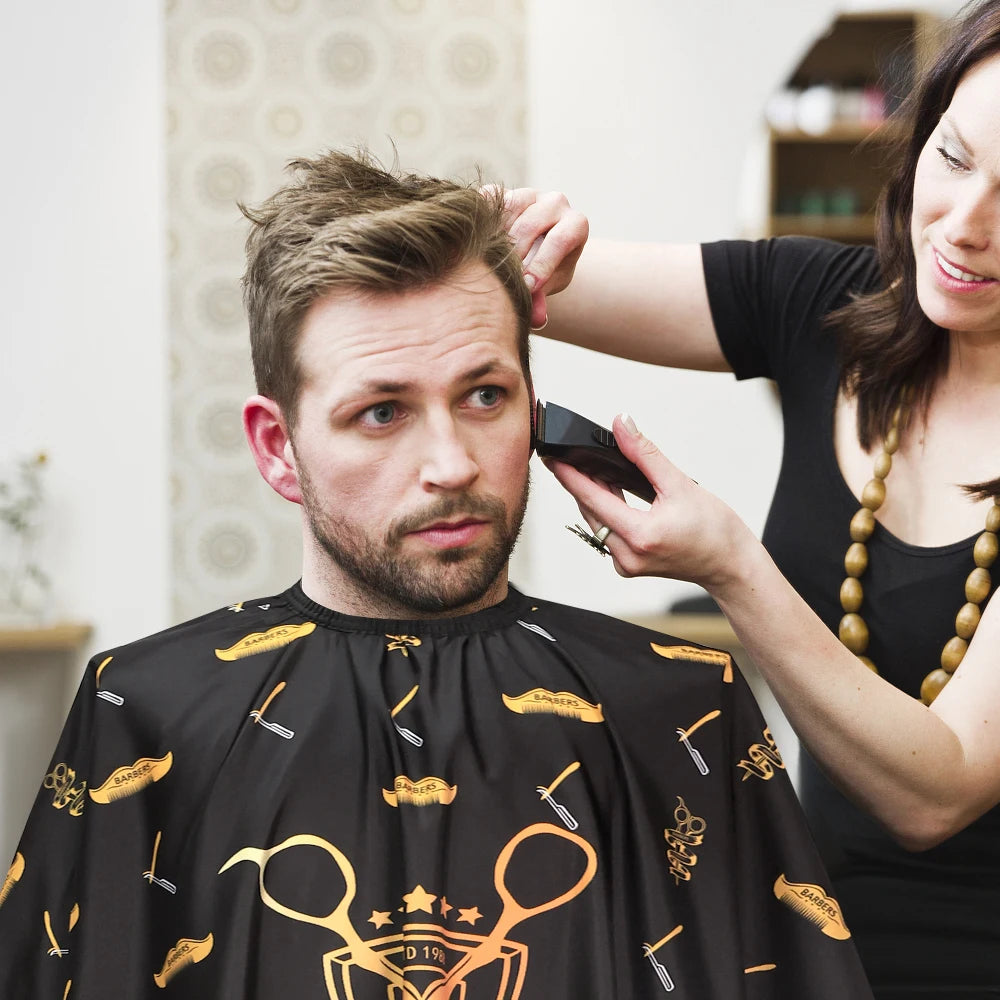 A woman is adjusting a black professional salon hair cutting cape on a man's chest.