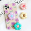 A light pink foldable phone grip stand featuring purple and green floral patterns with pastel colored flower accents.