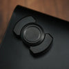 A close-up view of a black stainless steel fidget spinner and slider device resting on a dark surface.