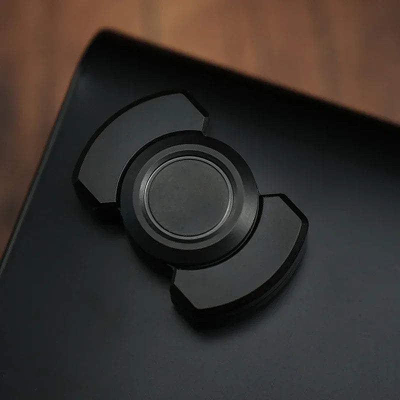 A close-up view of a black stainless steel fidget spinner and slider device resting on a dark surface.