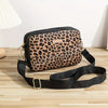 A black leopard print crossbody bag with a black strap resting on a wooden surface.