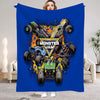 A blue flannel throw blanket featuring a cartoon design of monster trucks and a woman's face.