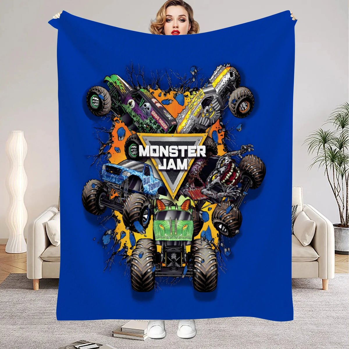 A blue flannel throw blanket featuring a cartoon design of monster trucks and a woman's face.