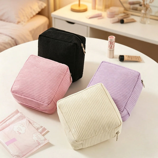 Bolsas de tela rosa, morada y beige para guardar toallas sanitarias y cosméticos sobre una mesa blanca.