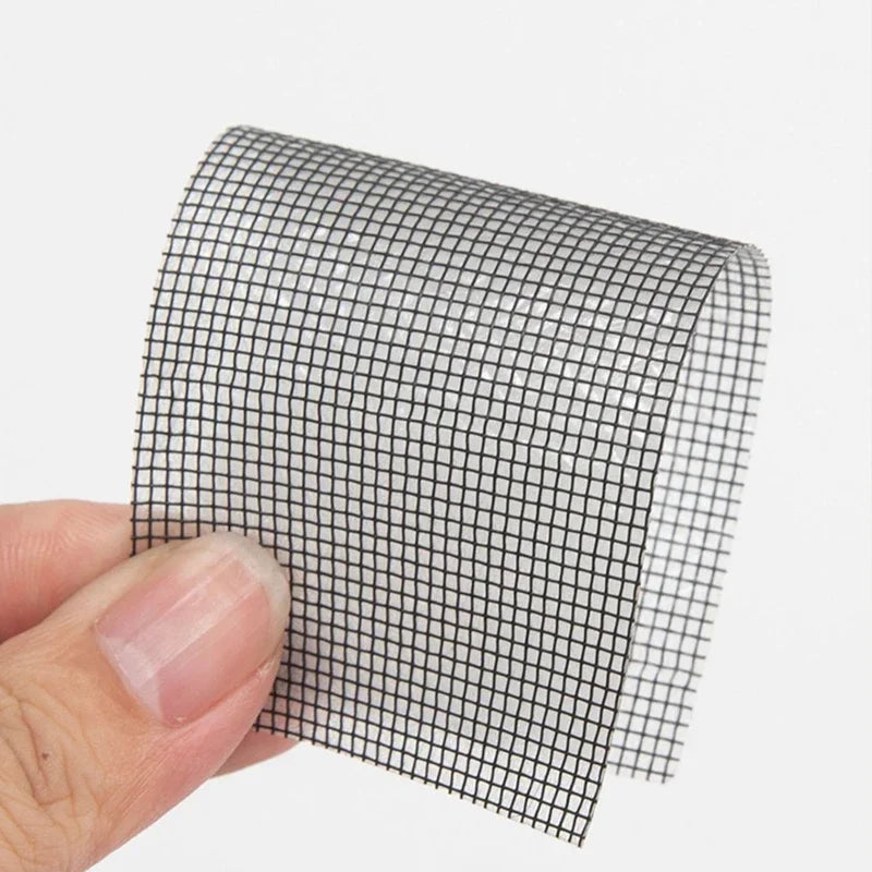 A hand is holding a self-adhesive black mesh repair patch for windows or screens.
