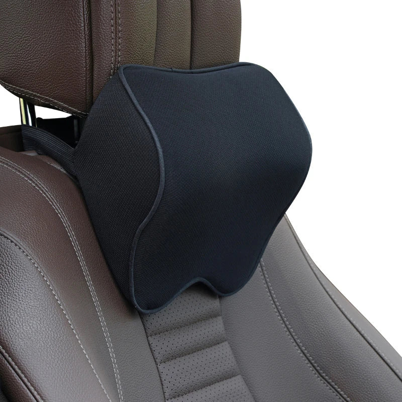 A black memory foam car headrest pillow is shown placed on a brown leather car seat.