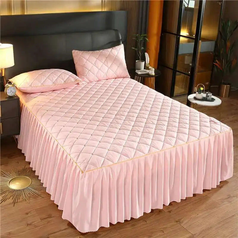Pink quilted bed skirt with a diamond pattern and gathered fabric on a bed.